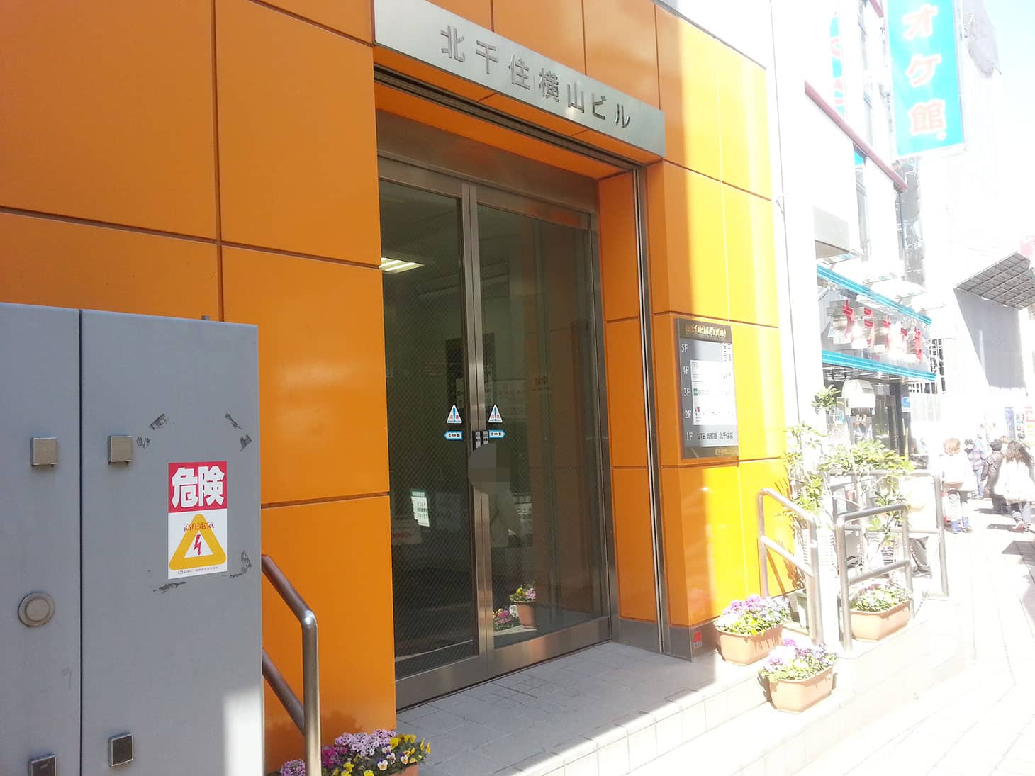 カラオケ館の隣の、「北千住横山ビル」の看板があるオレンジのビルが当社の入口です。